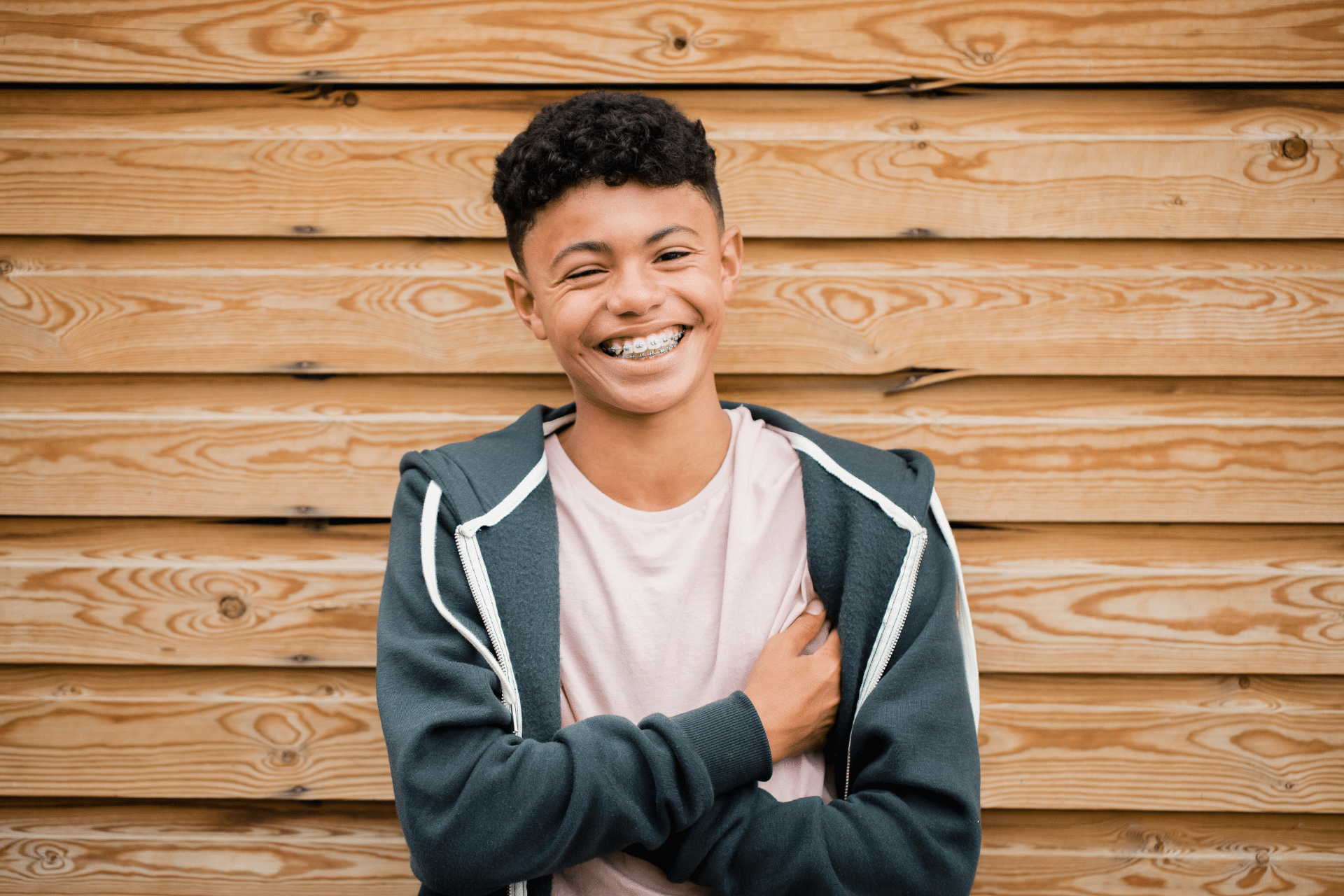 Smiling teen wearing braces with arms crossed against a wooden wall