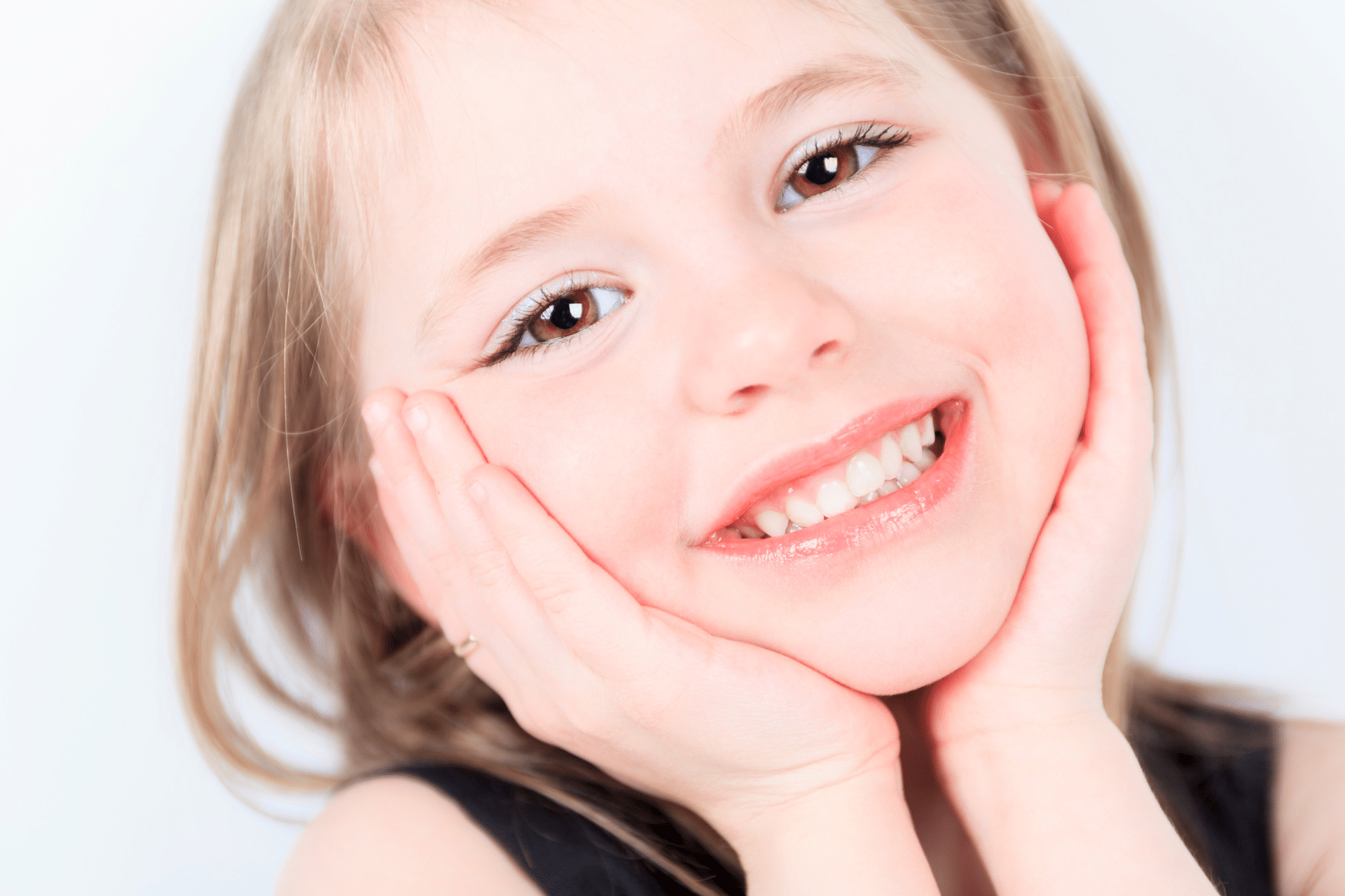 Close-up of a happy young girl resting her face in her hands and smiling brightly.