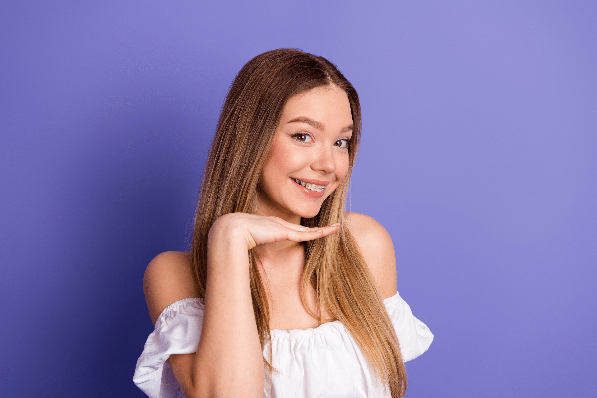 Smiling woman wearing clear braces against a purple background