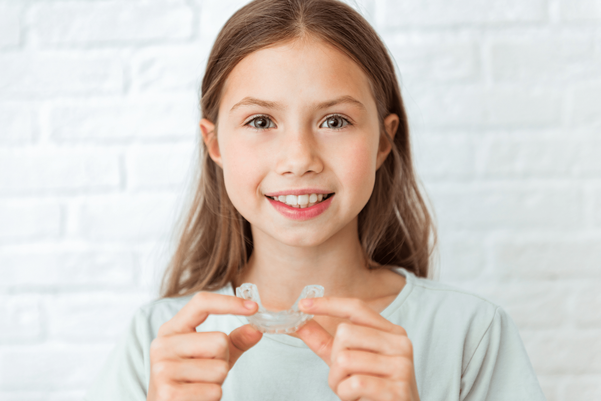A smiling young girl holding up a clear dental retainer.